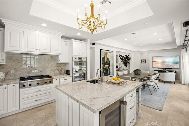 kitchen featuring sink, wine cooler, an island with sink, a tray ceiling, and stainless steel appliances