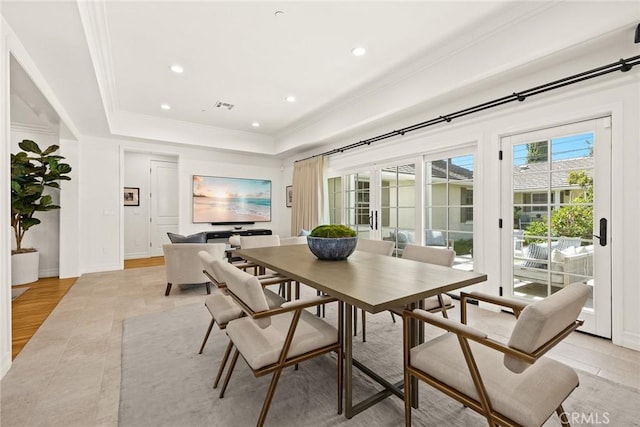 dining room featuring a raised ceiling, crown molding, and light wood-type flooring