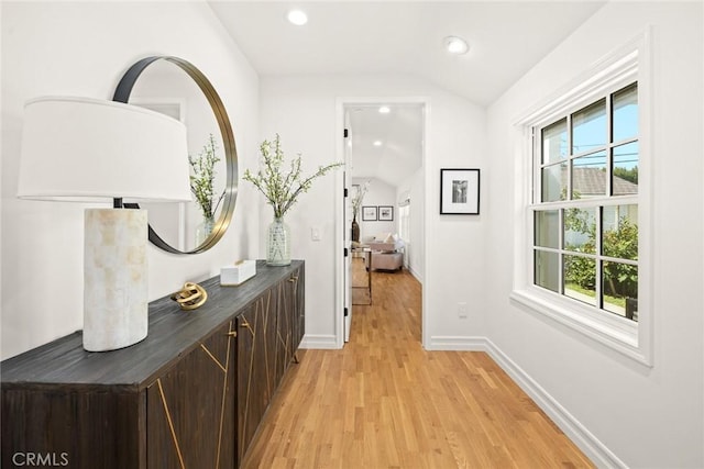 hallway with lofted ceiling, light hardwood / wood-style floors, and a healthy amount of sunlight