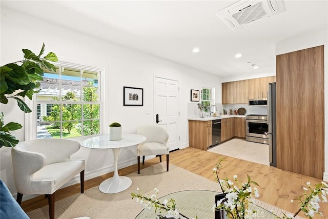 kitchen featuring decorative backsplash, kitchen peninsula, light wood-type flooring, stainless steel appliances, and sink