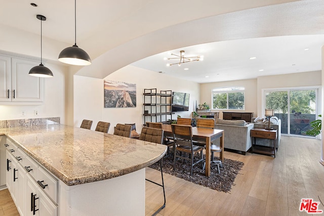 kitchen featuring white cabinetry, light stone counters, kitchen peninsula, a breakfast bar area, and light wood-type flooring