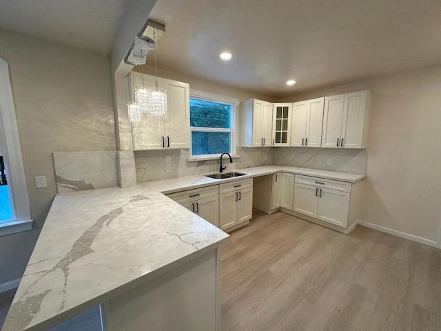 kitchen featuring kitchen peninsula, sink, light stone countertops, decorative light fixtures, and white cabinetry