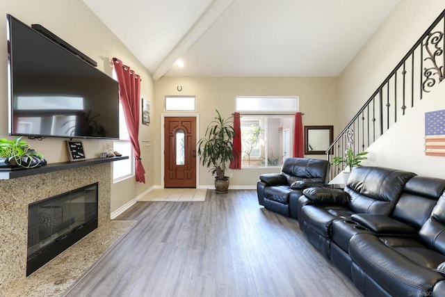 living room with lofted ceiling with beams, a healthy amount of sunlight, a premium fireplace, and light hardwood / wood-style flooring