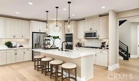 kitchen featuring appliances with stainless steel finishes, white cabinetry, light hardwood / wood-style flooring, decorative light fixtures, and a center island with sink