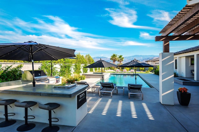 view of patio with a fenced in pool, a mountain view, grilling area, a pergola, and exterior kitchen