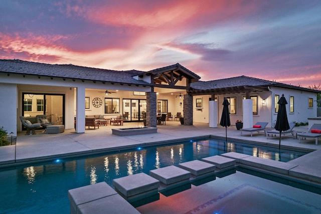 pool at dusk featuring an outdoor living space, an in ground hot tub, and a patio area