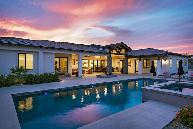 pool at dusk with an in ground hot tub and a patio area