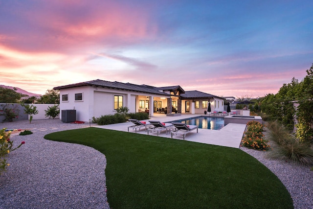 back house at dusk with cooling unit, a fenced in pool, a yard, and a patio area