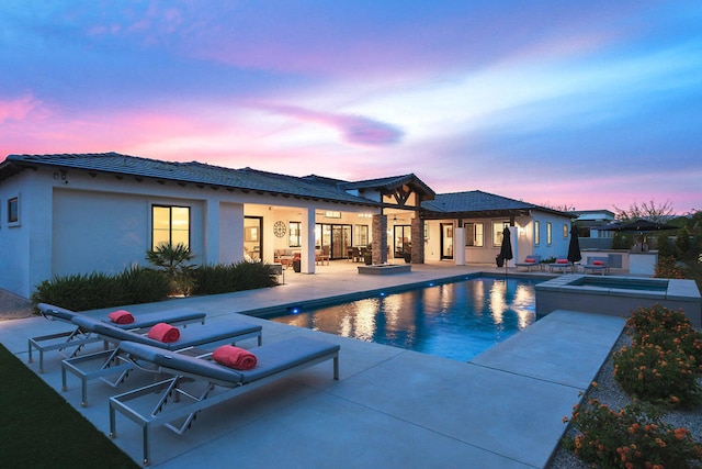 pool at dusk with a patio and an in ground hot tub