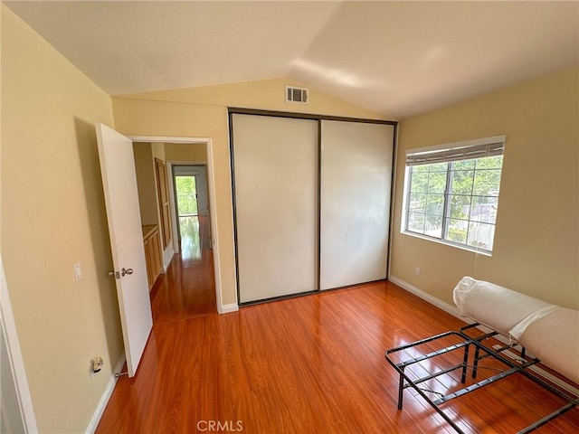 unfurnished bedroom with lofted ceiling, wood-type flooring, multiple windows, and a closet