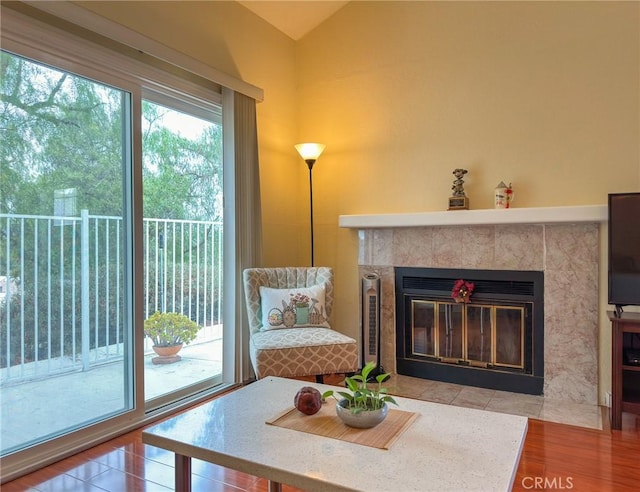 living room featuring wood-type flooring, vaulted ceiling, and a tiled fireplace