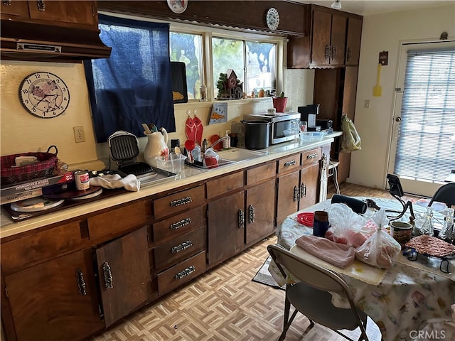 kitchen featuring sink, exhaust hood, light parquet floors, and dark brown cabinets