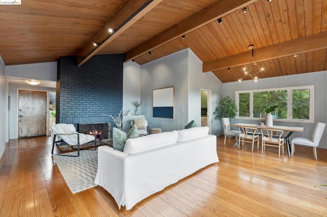 living room with vaulted ceiling with beams, light hardwood / wood-style floors, wood ceiling, and a brick fireplace