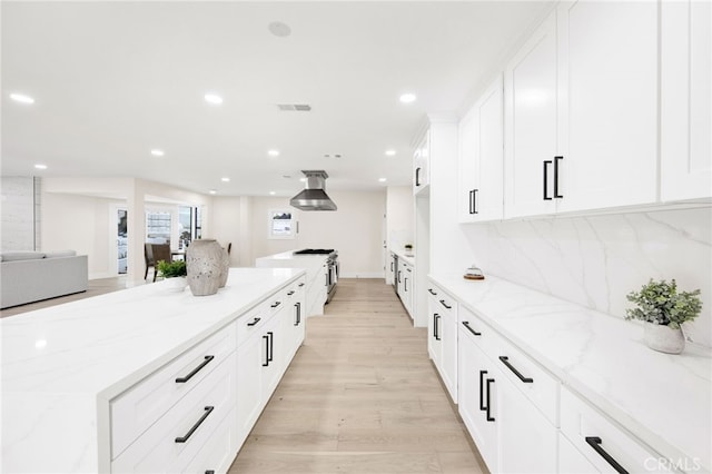 kitchen with light wood-type flooring, light stone counters, tasteful backsplash, ventilation hood, and white cabinetry