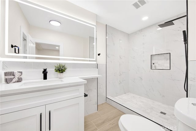 bathroom featuring a tile shower, vanity, and toilet