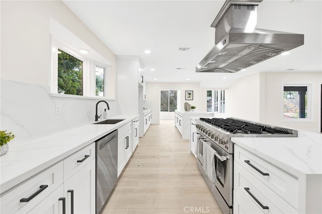 kitchen with white cabinets, appliances with stainless steel finishes, plenty of natural light, and range hood