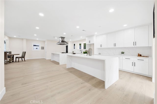 kitchen with white cabinets, an island with sink, sink, exhaust hood, and light wood-type flooring