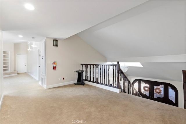 hallway with light colored carpet, built in shelves, and lofted ceiling with skylight