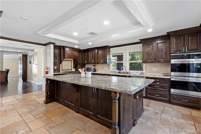 kitchen featuring crown molding, dark brown cabinets, stainless steel double oven, a kitchen bar, and a spacious island