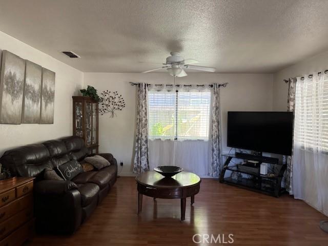 living room featuring ceiling fan, dark hardwood / wood-style flooring, and a textured ceiling