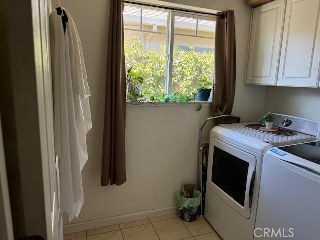 laundry area featuring washing machine and clothes dryer, light tile patterned floors, and cabinets