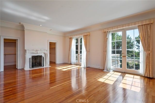 unfurnished living room with light hardwood / wood-style flooring, ornamental molding, a high end fireplace, and french doors