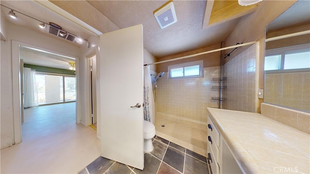 bathroom featuring ceiling fan, vanity, a textured ceiling, a tile shower, and toilet