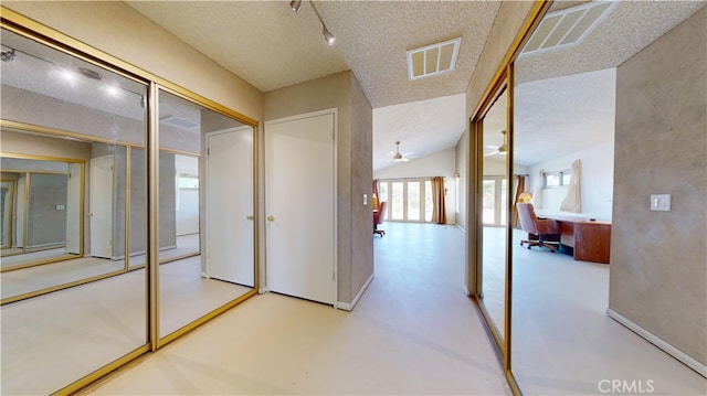 corridor featuring a textured ceiling, lofted ceiling, and track lighting