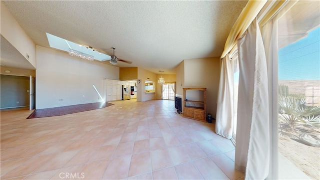 unfurnished living room with ceiling fan, a skylight, a textured ceiling, and light tile patterned flooring