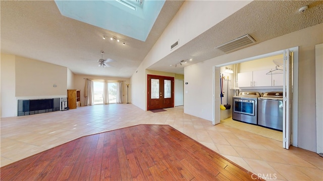 unfurnished living room with vaulted ceiling, independent washer and dryer, light tile patterned floors, a textured ceiling, and ceiling fan