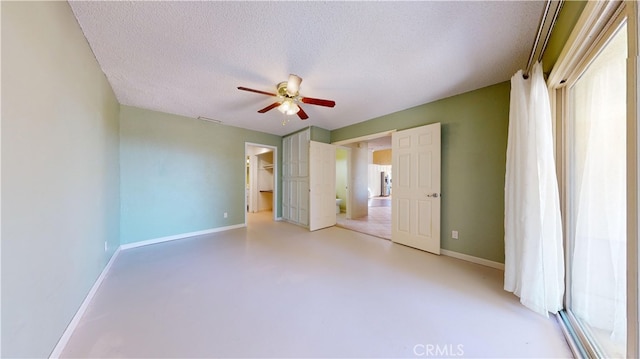 unfurnished bedroom with a closet, a textured ceiling, a walk in closet, and ceiling fan