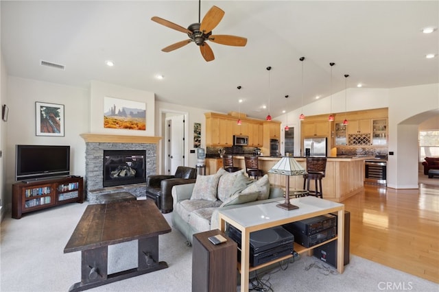 living room with wine cooler, vaulted ceiling, light hardwood / wood-style flooring, a stone fireplace, and ceiling fan