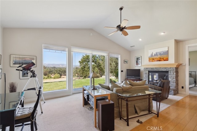 living room with ceiling fan, vaulted ceiling, a fireplace, and light hardwood / wood-style floors