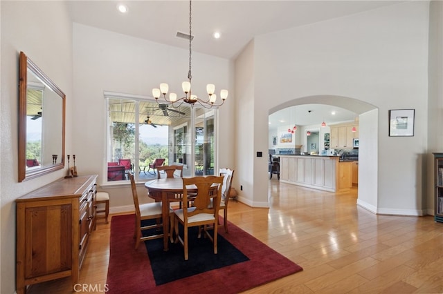 dining space featuring a towering ceiling, an inviting chandelier, and light hardwood / wood-style flooring