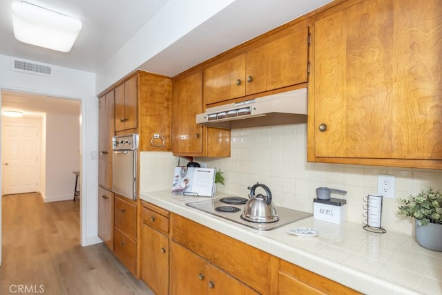 kitchen with tile countertops, decorative backsplash, light wood-type flooring, and stainless steel appliances