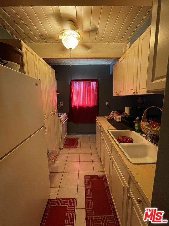 kitchen with white cabinetry, sink, white appliances, light tile patterned floors, and wood ceiling