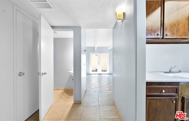 hall featuring light tile patterned flooring, sink, a textured ceiling, and french doors