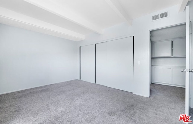 unfurnished bedroom featuring beamed ceiling and light carpet