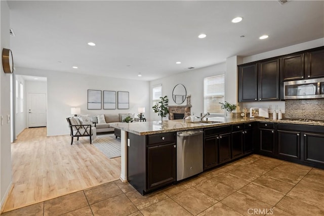 kitchen featuring kitchen peninsula, backsplash, stainless steel appliances, sink, and light hardwood / wood-style flooring