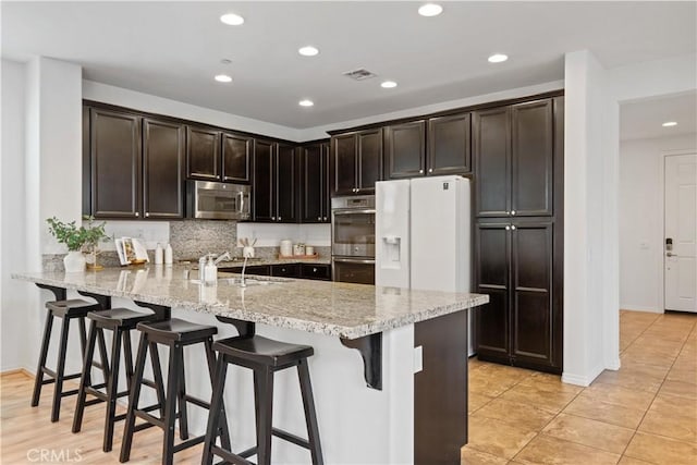 kitchen featuring kitchen peninsula, appliances with stainless steel finishes, dark brown cabinetry, and light stone countertops