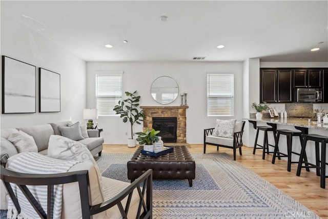 living room with a stone fireplace, a healthy amount of sunlight, and light hardwood / wood-style floors