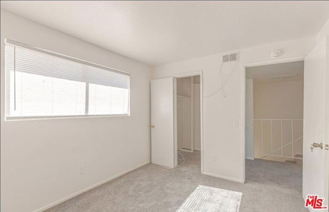 unfurnished bedroom with multiple windows, a walk in closet, and light colored carpet