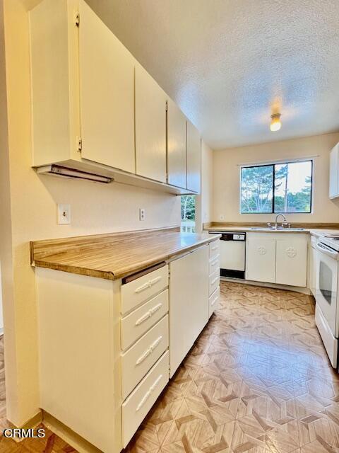 kitchen with sink, white appliances, white cabinetry, and a textured ceiling