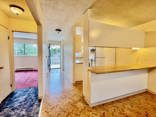 kitchen featuring white fridge, white cabinetry, a textured ceiling, and a baseboard radiator