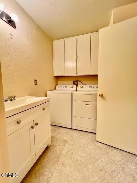 laundry room featuring washing machine and dryer, sink, cabinets, and a textured ceiling