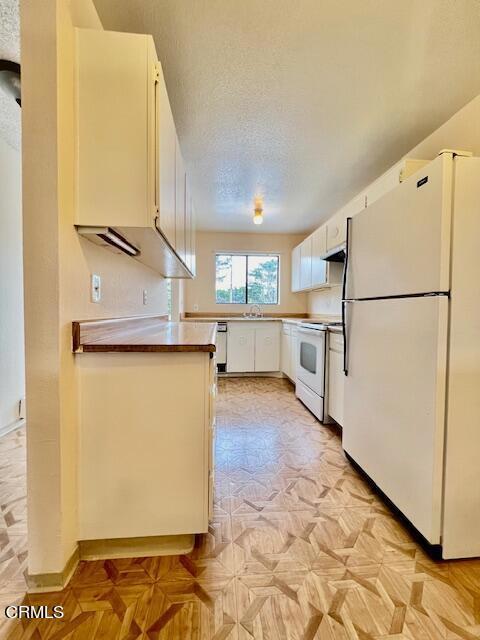 kitchen with white cabinets, a textured ceiling, white appliances, and sink