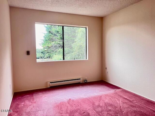 carpeted spare room with a textured ceiling and a baseboard heating unit