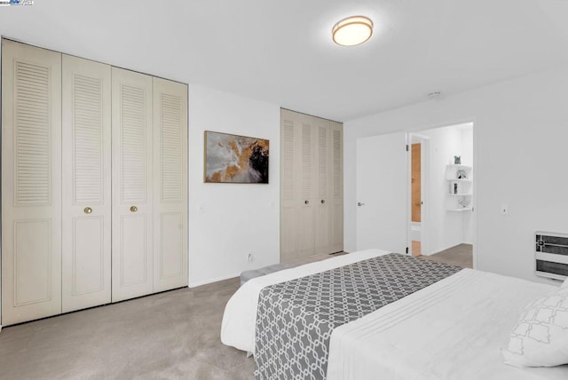 bedroom featuring light carpet, two closets, and heating unit