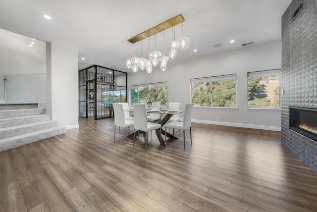 dining space with a tiled fireplace, a chandelier, and hardwood / wood-style flooring