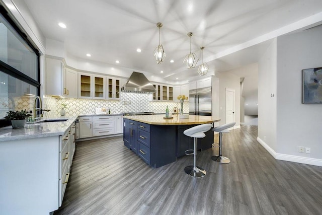 kitchen featuring blue cabinetry, white cabinetry, wall chimney range hood, a kitchen island, and appliances with stainless steel finishes